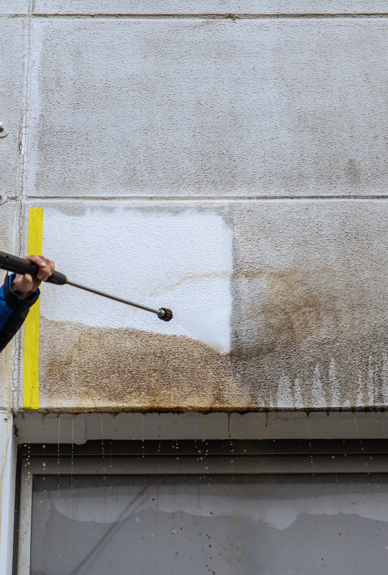 Das Bild zeigt einen Mitarbeiter der Firma Albo-Servie, der eine Probereinigung an einer Fassade durchführt.